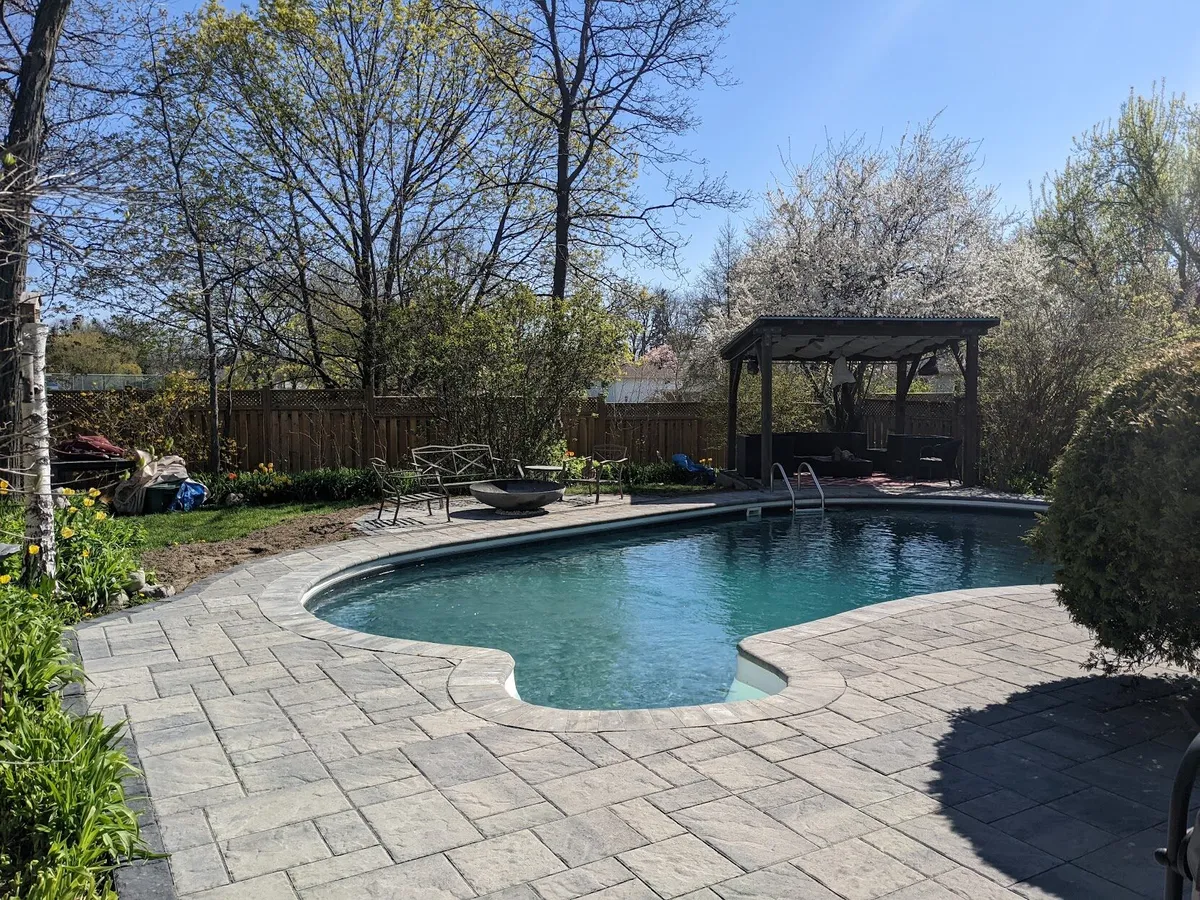 A beautiful backyard with a pool, gazebo, and firepit using a modern, but slate textured interlock
