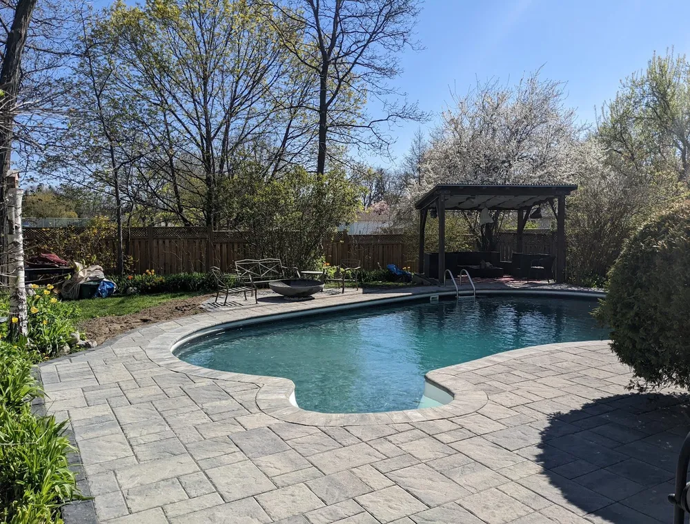 A beautiful backyard with a pool, gazebo, and firepit using a modern, but slate textured interlock