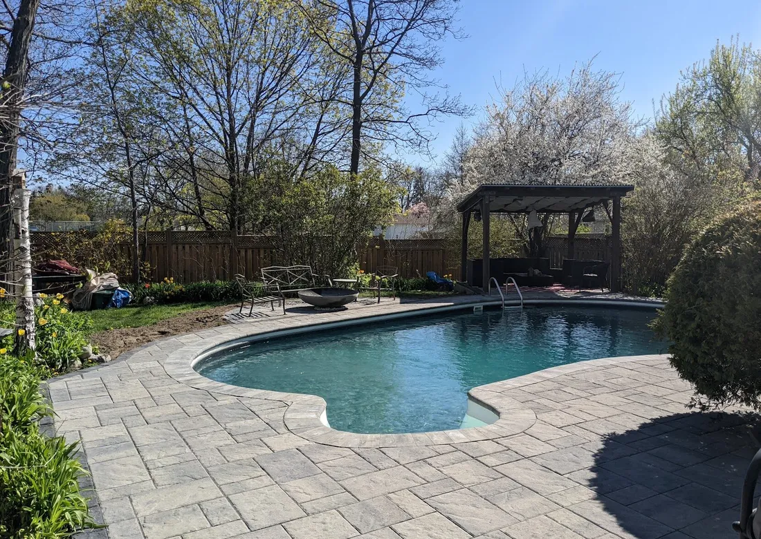 A beautiful backyard with a pool, gazebo, and firepit using a modern, but slate textured interlock