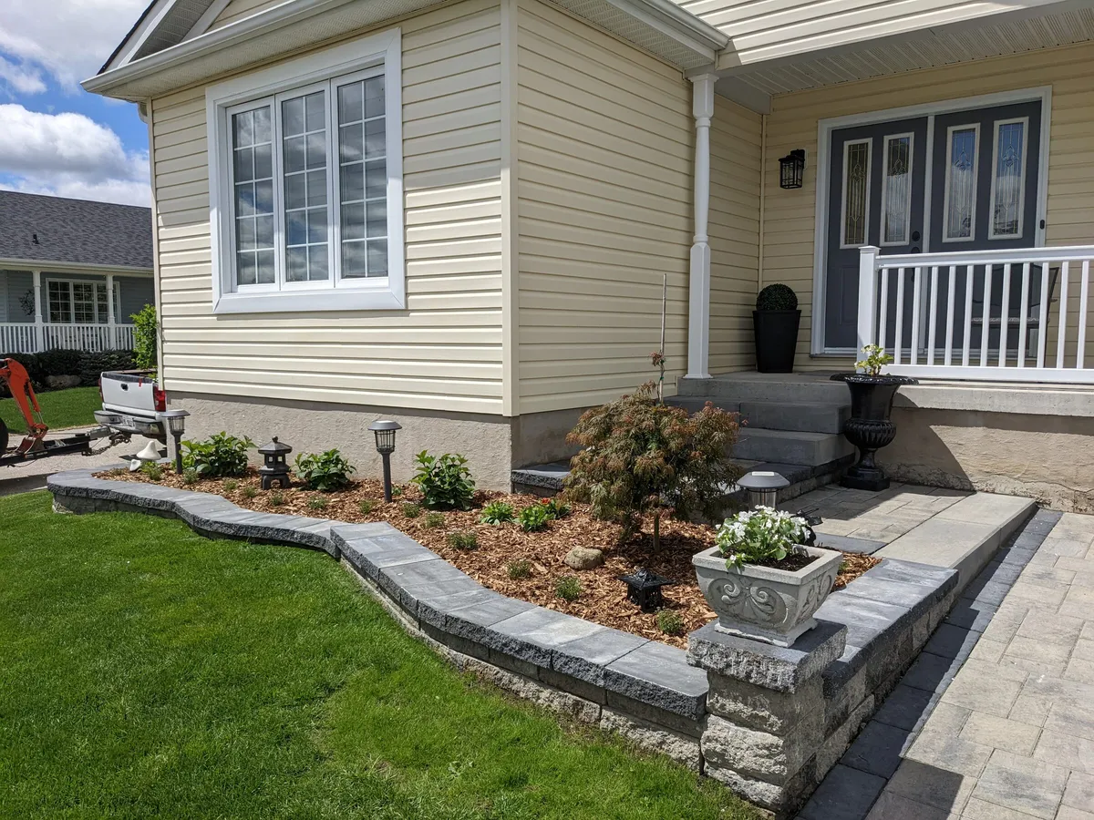 A beautiful natural garden wall supporting a well-placed set of plants and solar lights. The garden wraps around a house and an interlock front landing with numerous steps