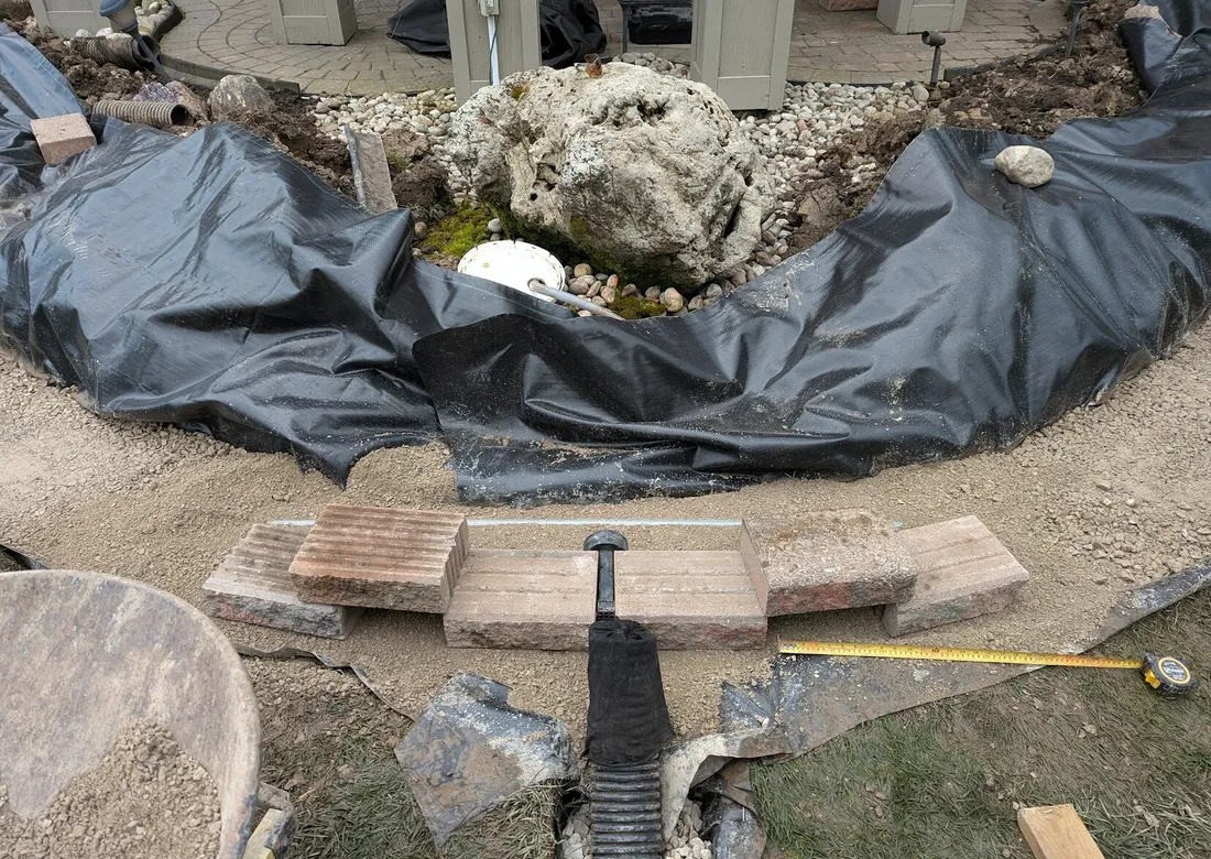 A wall system being installed on top of bedding, with a drainage system in the center inserted into the wall, and leading out into a front weeping tile